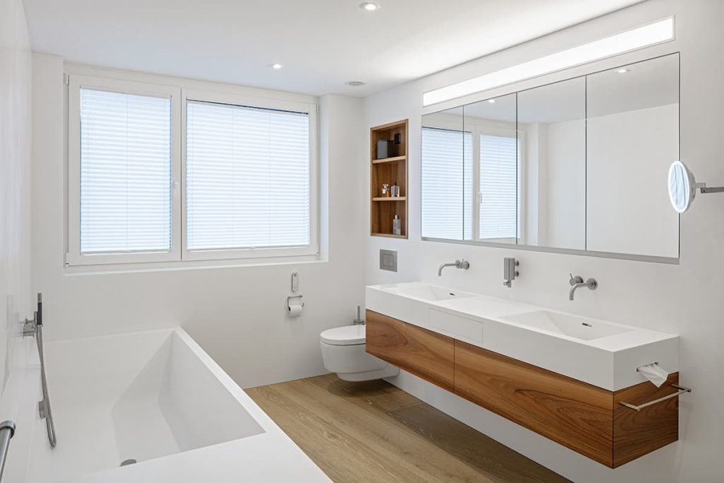 Badmöbel mit weissem Doppelwaschtisch, Holzfront, Einbaunische und Spiegelschrank neben der Badewanne – Zeiter + Berchtold, Brig-Glis