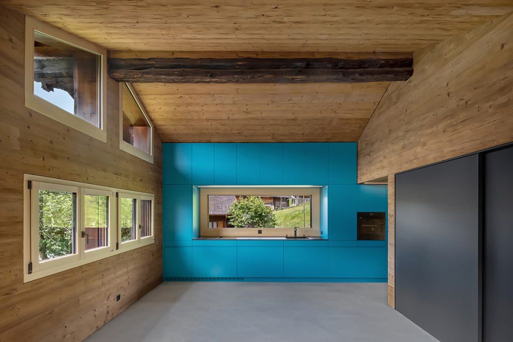 Raum mit Holzwänden und Holzdecke, Balken und türkisfarbener Wand mit Fensterband – Zeiter + Berchtold, Brig-Glis