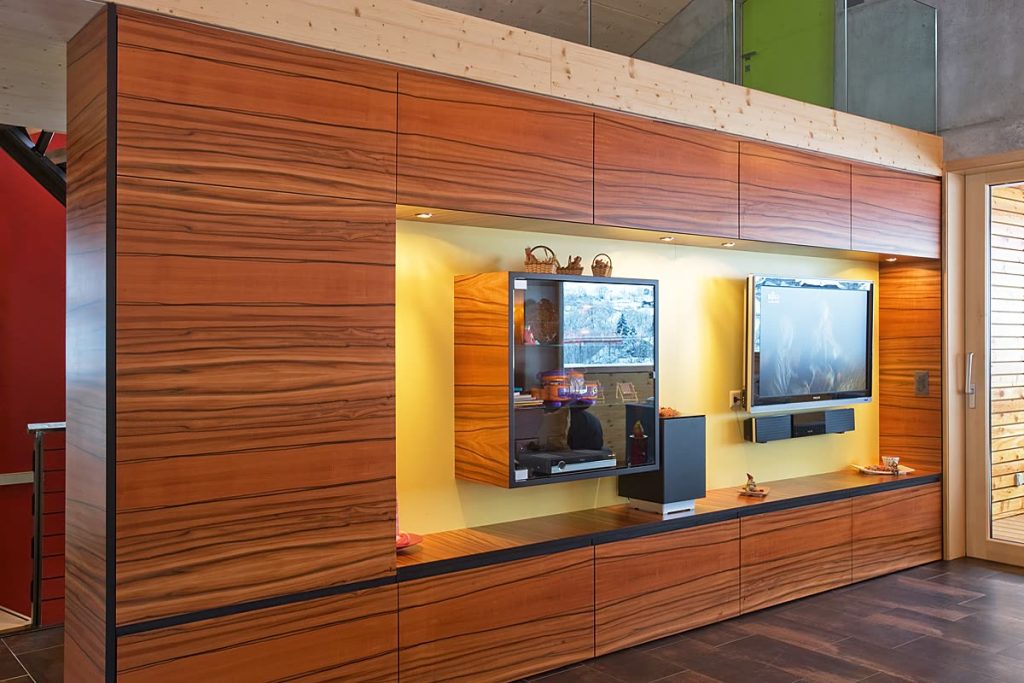 Wohnwand aus gestreiftem Holz mit gelb hinterlegter Nische für Fernseher und Vitrine
