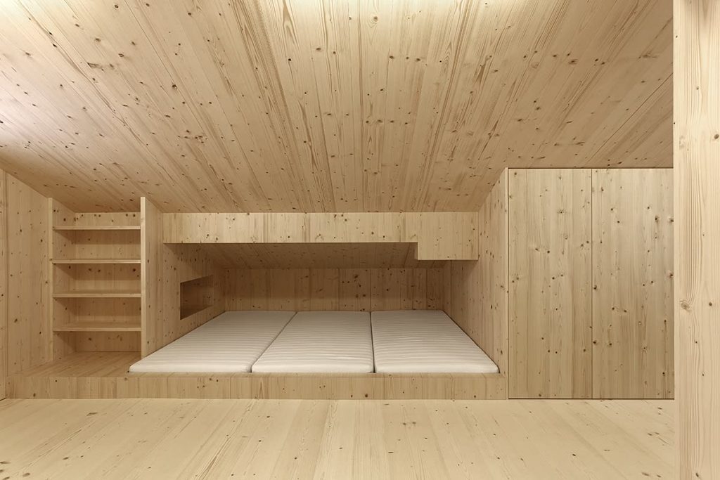 Dachraum aus hellem Massivholz mit eingebauter Liegefläche, Regal und Einbauschränken