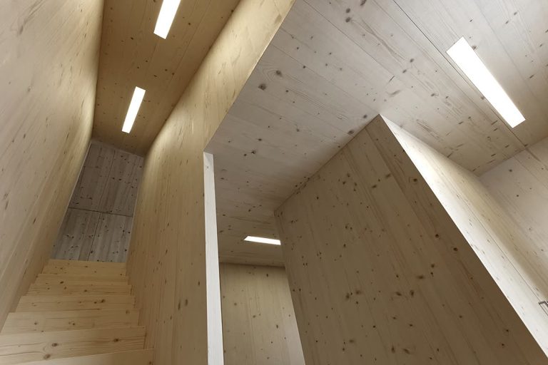 Treppenhaus mit Wänden aus hellem Massivholz und eingelassenen Lichtbändern