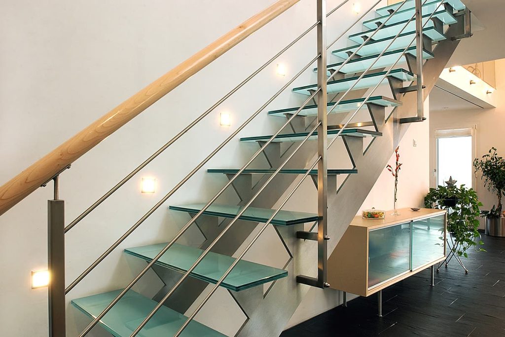 Treppe mit Glasstufen, Edelstahlgeländer und Holzhandlauf, daneben Sideboard