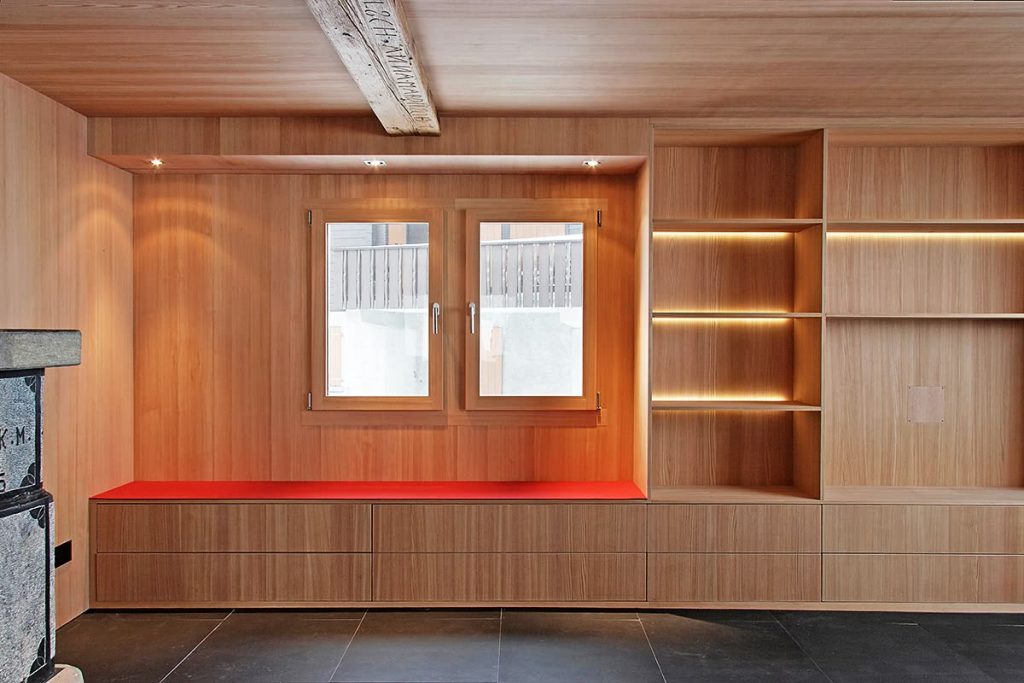 Holzverkleidete Wand mit beleuchteten Regalfächern und Sitzbank mit rotem Polster