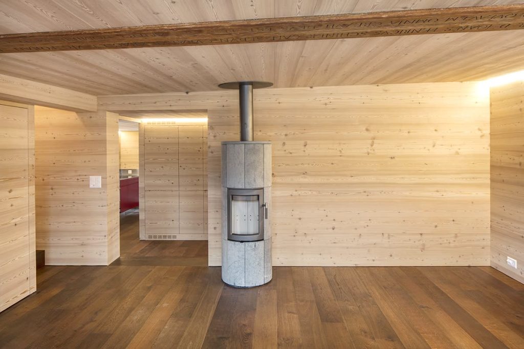 Wohnraum mit heller Holzverkleidung, Specksteinofen, Holzbalken und dunklem Parkett