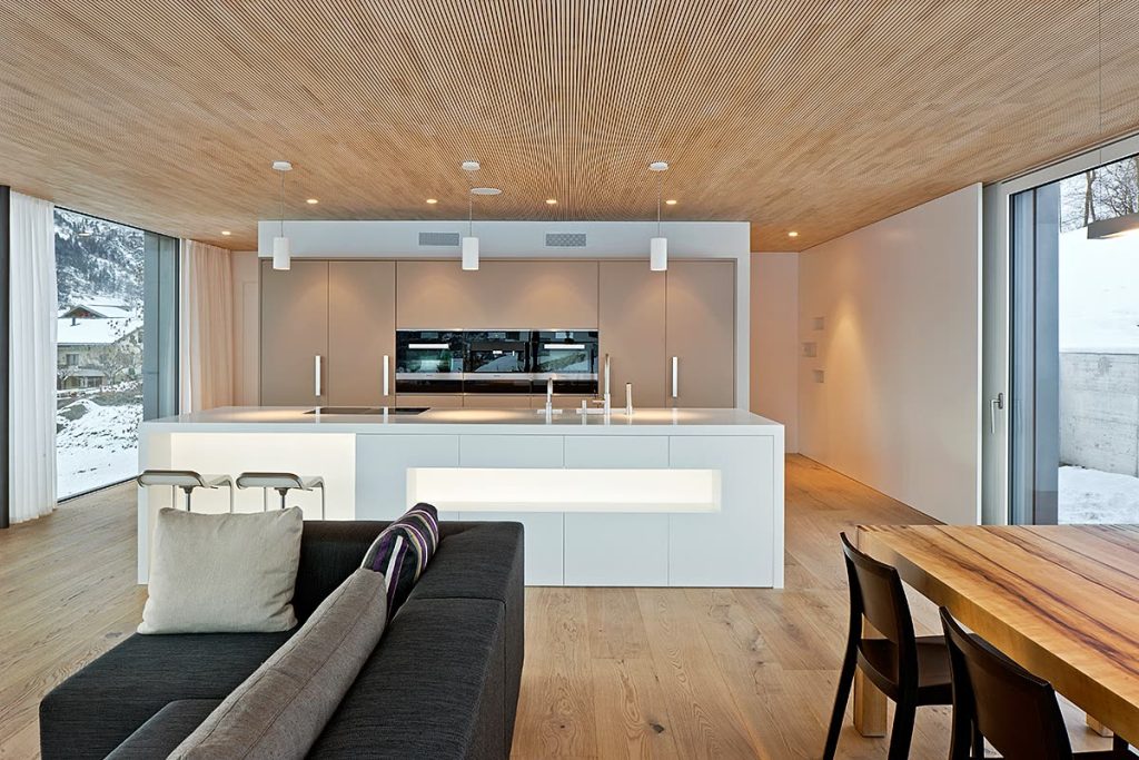 Offener Wohn- und Küchenbereich mit weisser Insel, Sofa und Esstisch aus Holz