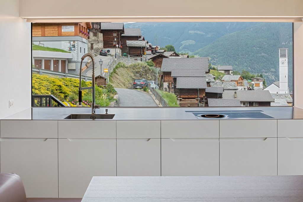 Weisse Küche mit grossem Fenster und Blick auf ein Walliser Dorf