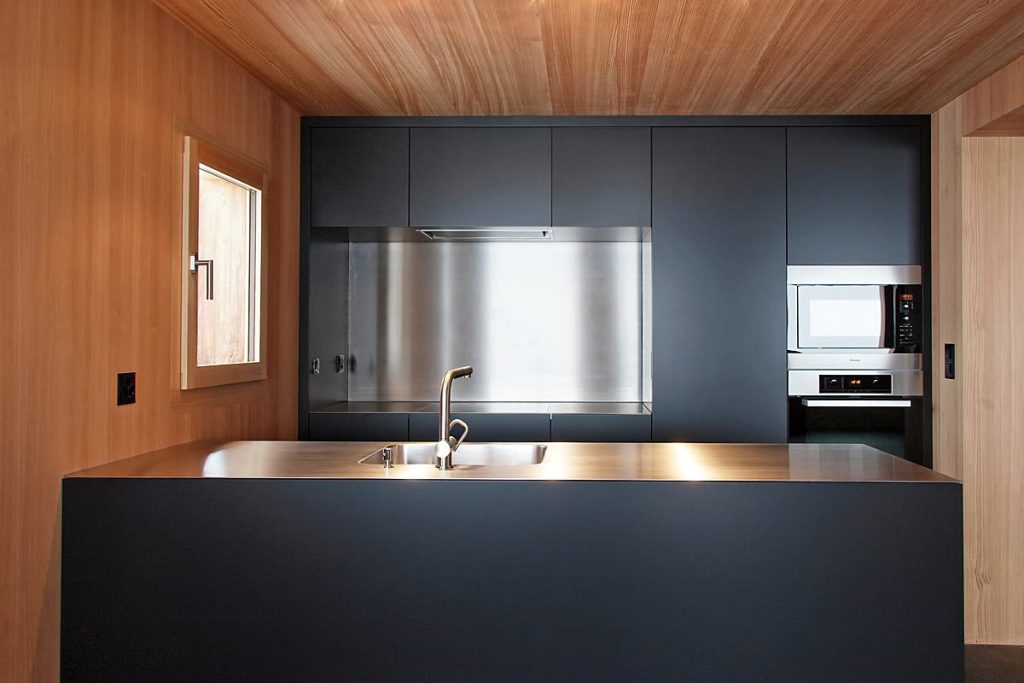 Küche mit schwarzen Fronten und Edelstahl-Rückwand in einem Raum mit Holzverkleidung