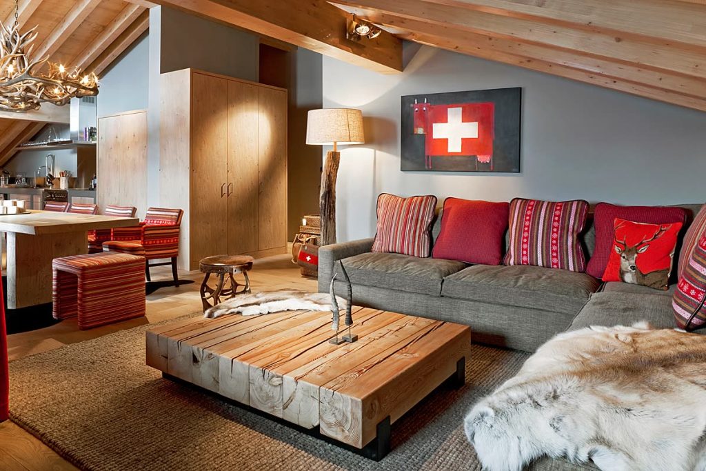 Wohnzimmer im Chalet mit Altholz-Salontisch, Sofa mit roten Kissen und Holzschränken