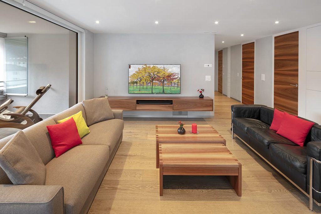 Wohnzimmer mit Salontisch aus Streifenholz, Sofas, TV-Möbel und Türen in Nussbaum – Zeiter + Berchtold, Brig-Glis