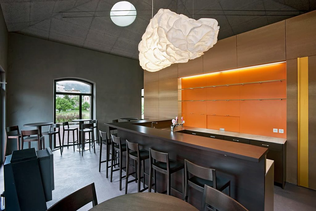 Bar mit dunkler Theke, orangefarbener Rückwand, Barhockern und Wolkenleuchte