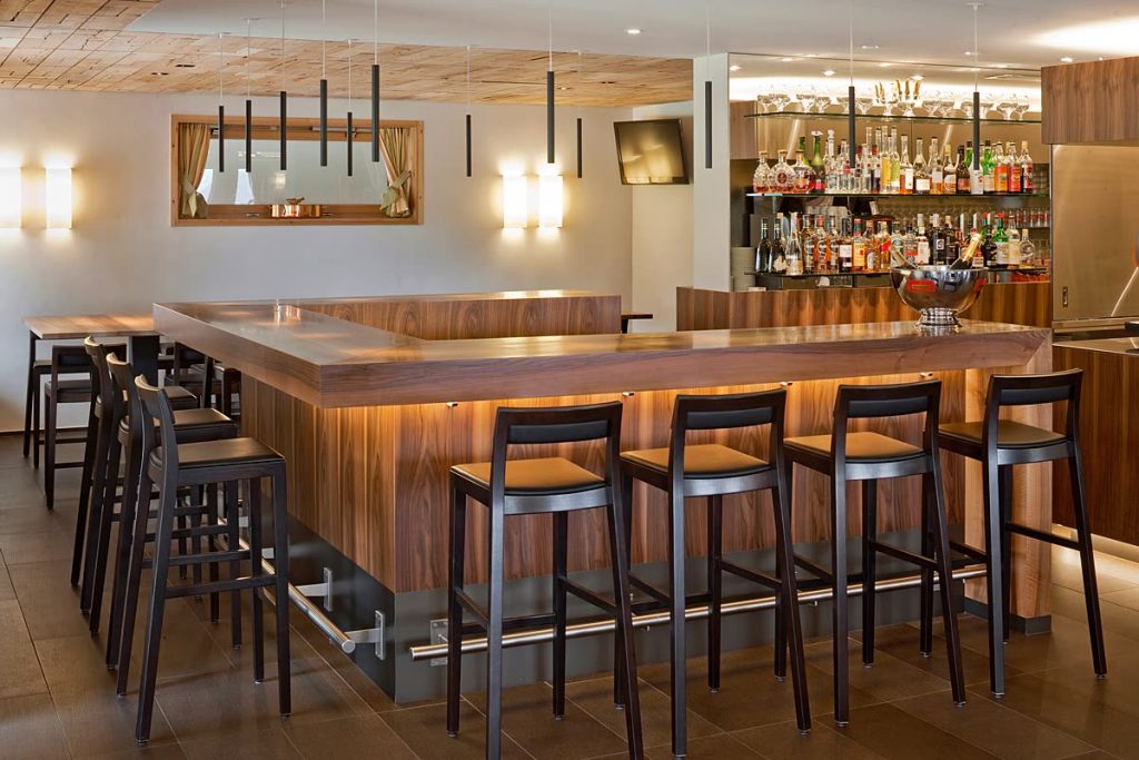 Bar im Restaurant mit Theke aus Holz, Barhockern und beleuchteter Flaschenwand