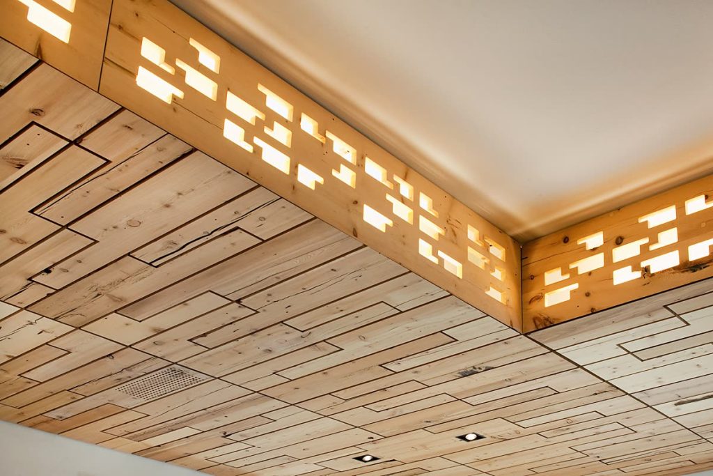 Decke aus Altholz mit beleuchtetem Lichtfries aus durchbrochenem Holz