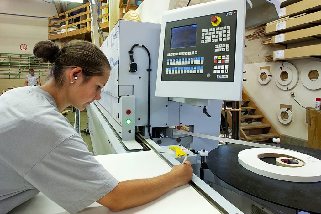 Mitarbeiterin bedient eine Kantenanleimmaschine in der Werkstatt