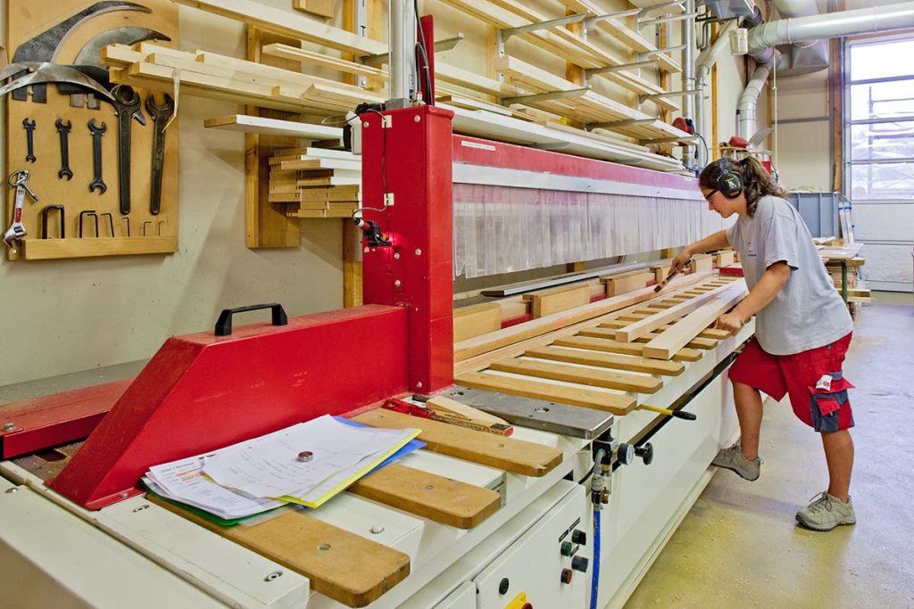 Mitarbeiterin an einer Plattenmaschine in der Werkstatt mit Werkzeugwand